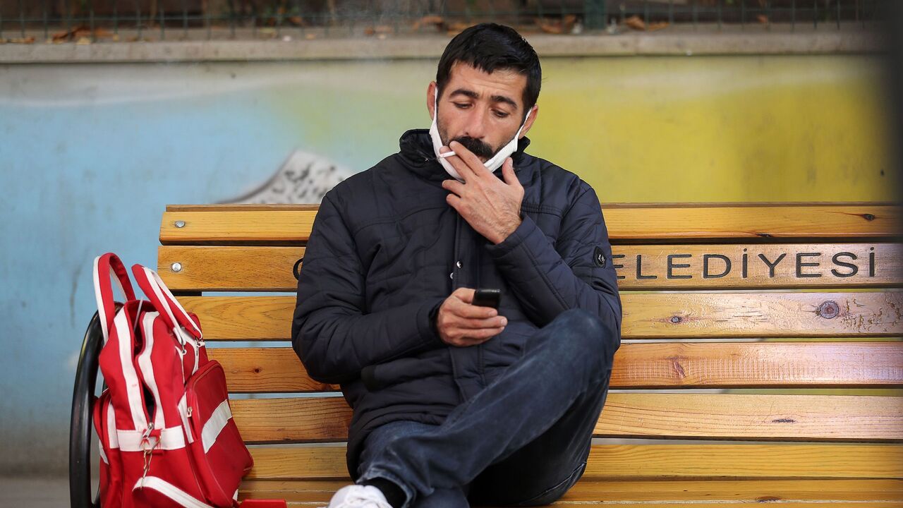 1229604954 A man sitting on a public bench smokes a cigarette while using his mobile phone in Ankara on November 13, 2020, after Turkey banned smoking in outdoor public areas as part of restrictions aimed at curbing the spread of the Covid-19 pandemic, caused by the novel coronavirus. - Turkey on November 11, 2020, announced a ban on smoking across the country in a number of outdoor spaces including crowded streets, public squares and transport stops, in a bid to limit rising Covid-19 infections. The ban was issued o
