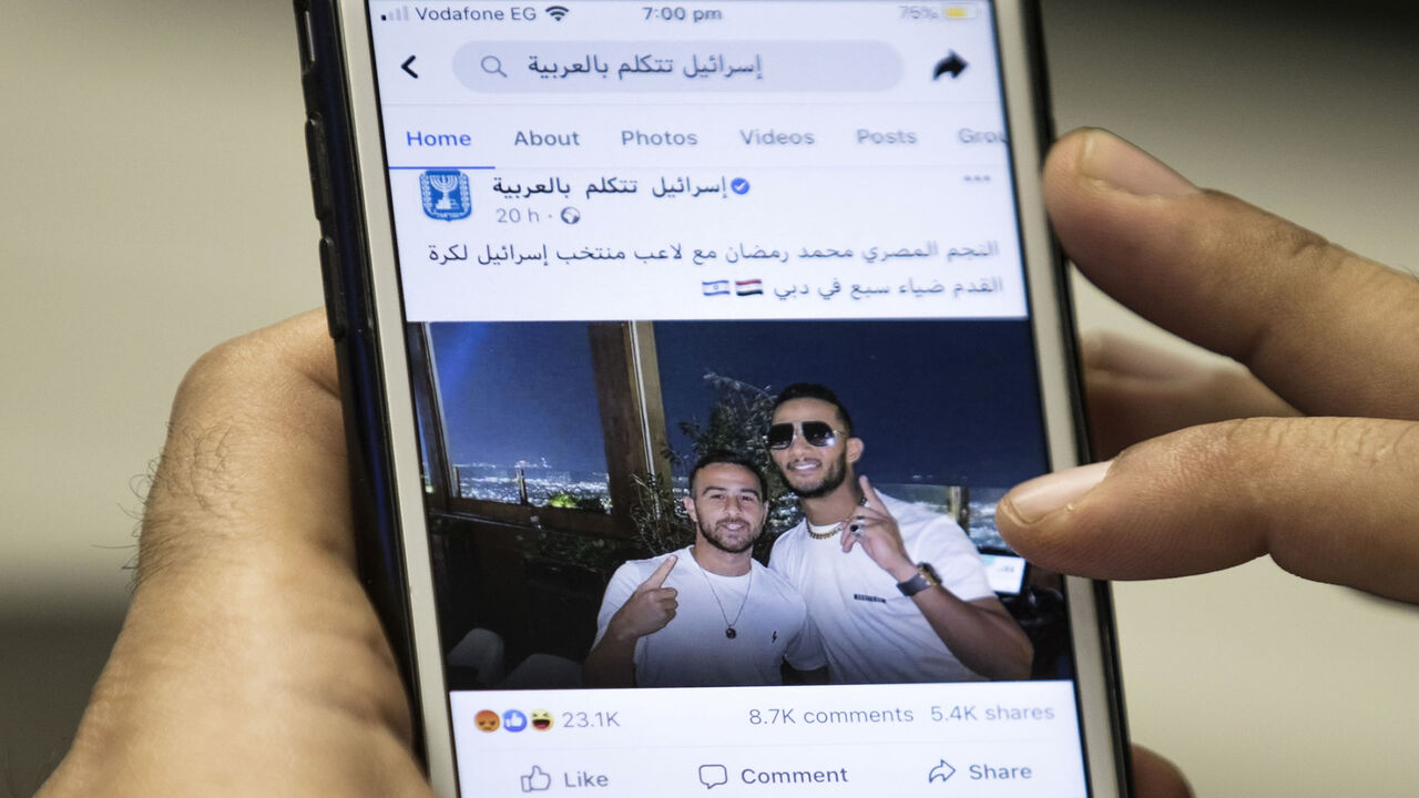 1229737218 This picture taken on November 22, 2020 in Cairo shows a man holding a phone showing a picture of Egypt's self-proclaimed "superstar" Mohamed Ramadan posted by the official Facebook page of the State of Israel in Arabic (linked to the foreign ministry) depicting Ramadan (R) hugging Israeli midfielder Dia Saba in Dubai. - Ramadan, a 32-year-old actor and rapper, boasts millions of followers in the Arab world, is a close friend of Morocco's King Mohamed VI and the recipient of the 2019 All Africa Music Awards