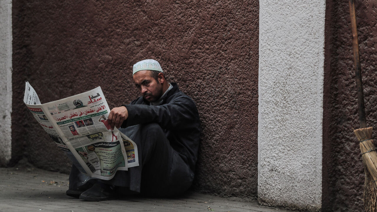 1188834562 A man reads a newspaper on a sidewalk in the Zamalek district of western Cairo on December 15, 2019. (Photo by Mohamed el-Shahed / AFP) (Photo by MOHAMED EL-SHAHED/AFP via Getty Images)