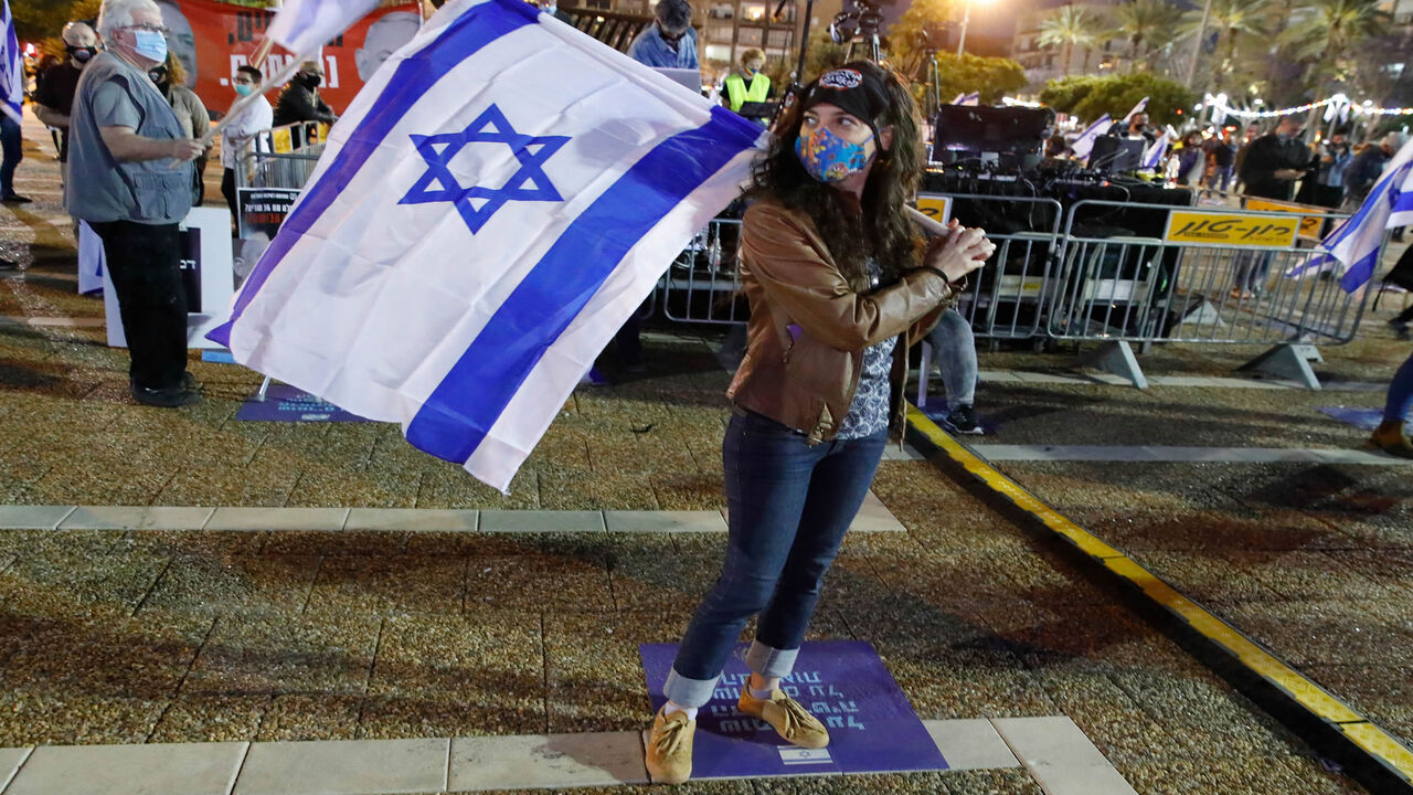 1211621202 An Israeli woman wearing a protective mask carries a national flag as she takes part in a demonstration in Tel Aviv's Rabin Square on May 2, 2020, in favour of the Supreme Court to consider tomorrow to block the coalition government agreed between Prime Minister Benjamin Netanyahu and his rival-turned-partner Benny Gantz. - If the expanded panel of 11 judges set to hear the case deems the coalition deal invalid, Israel may be forced to hold its fourth election in less than two years. (Photo by JACK GUEZ / A