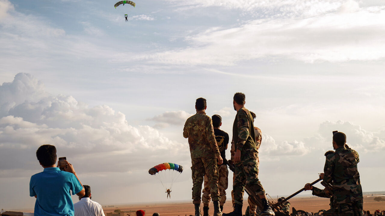1229492438 Attendees watch as a paratrooper makes a landing during an event by members of the the "Saiqa" (Special Forces) of the self-proclaimed Libyan National Army (LNA), loyal to eastern strongman Khalifa Haftar, in tribute to the unit's late commander General Wanis Bukhamada, who died a week prior, in the eastern city of Benghazi on November 6, 2020. (Photo by Abdullah DOMA / AFP) (Photo by ABDULLAH DOMA/AFP via Getty Images)