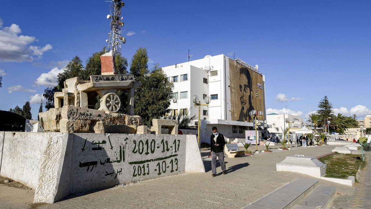 1229987725 A man walks past a sculpture of Mohamed Bouazizi's cart (bearing text reading in Arabic: "I do not forgive") in the square named after him in the centre of the town of Sidi Bouzid in central Tunisia on October 27, 2020, the cradle of the 2011 Tunisian revolution where unemployment remains high ten years later. - The sister of Mohamed Bouazizi, whose self-immolation sparked a string of Arab uprisings, says she is "very disappointed" in Tunisia's revolution and has urged young Tunisians to continue the fight