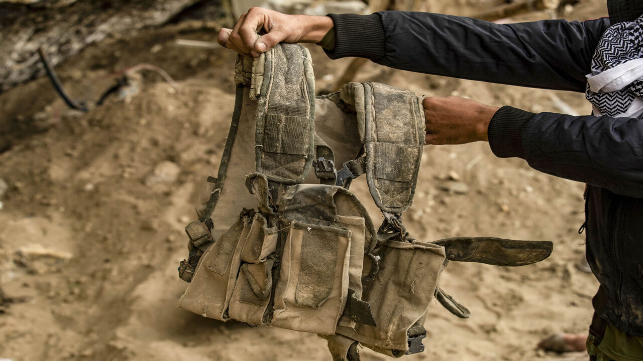 1207749338 A fighter from the Syrian Democratic forces (SDF) carries a military vest said to have belonged to Islamic State (IS) group jihadists, recovered in the eastern Syrian village of Baghuz on March 13, 2020, a year after the fall of the Islamic State's (IS) caliphate. - A year after the last black flag of the Islamic State group was lowered in the Syrian village of Baghouz, traces of the jihadist group are still all around this small and remote village near the Iraqi border, where Kurdish fighters and the US-le