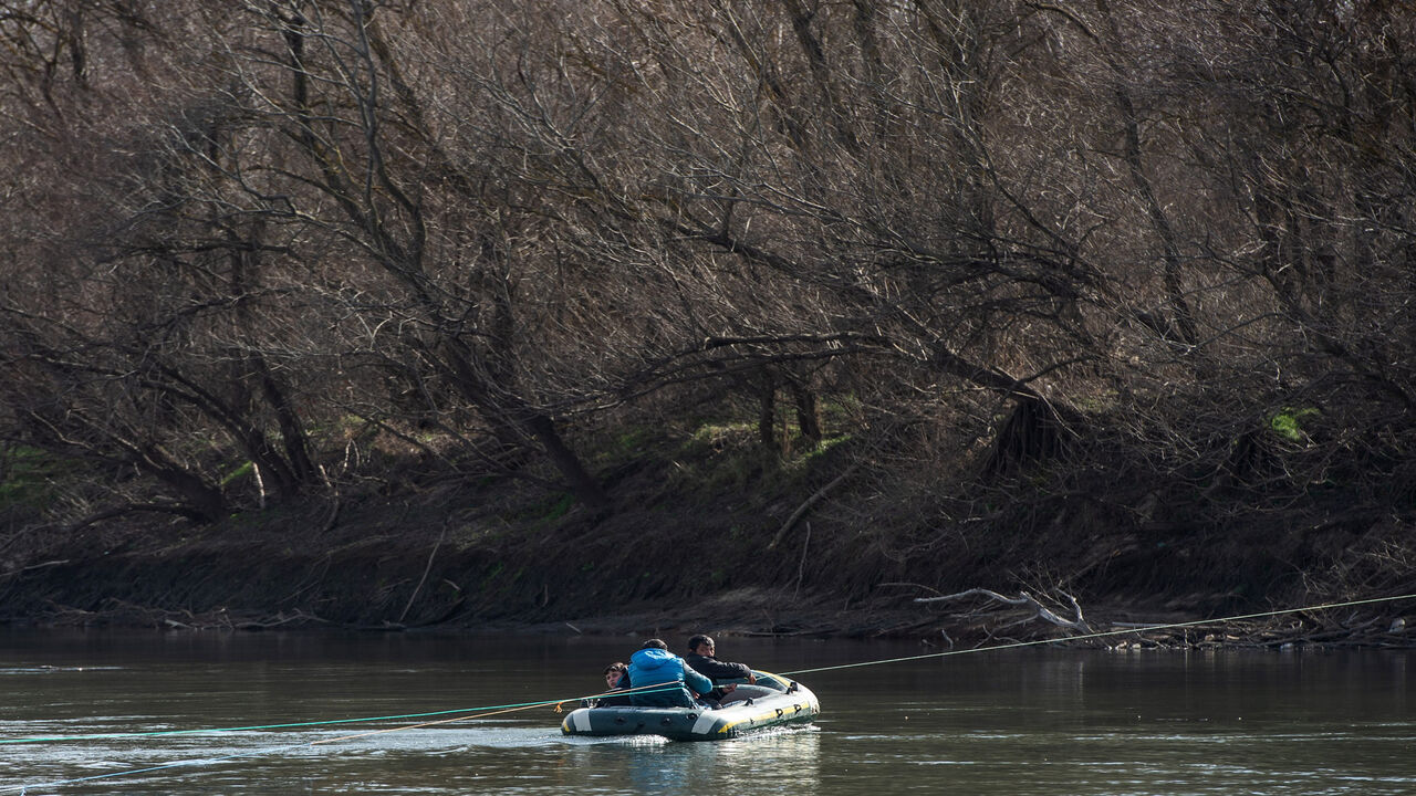 1209920048 EDIRNE, TURKEY - MARCH 02: Three men hold a rope as they travel in an inflatable boat as they attempt to enter Greece from Turkey by crossing the Evros river on on March 02, 2020 in Edirne, Turkey. Thousands of refugees and migrants have flocked to the Greece, Turkey border after Turkey announced that it would open border gates for a period of 72hrs to allow refugees to cross into European countries after thirty three Turkish soldiers were killed in a Syrian air raid in Idlib. (Photo by Burak Kara/Getty Im