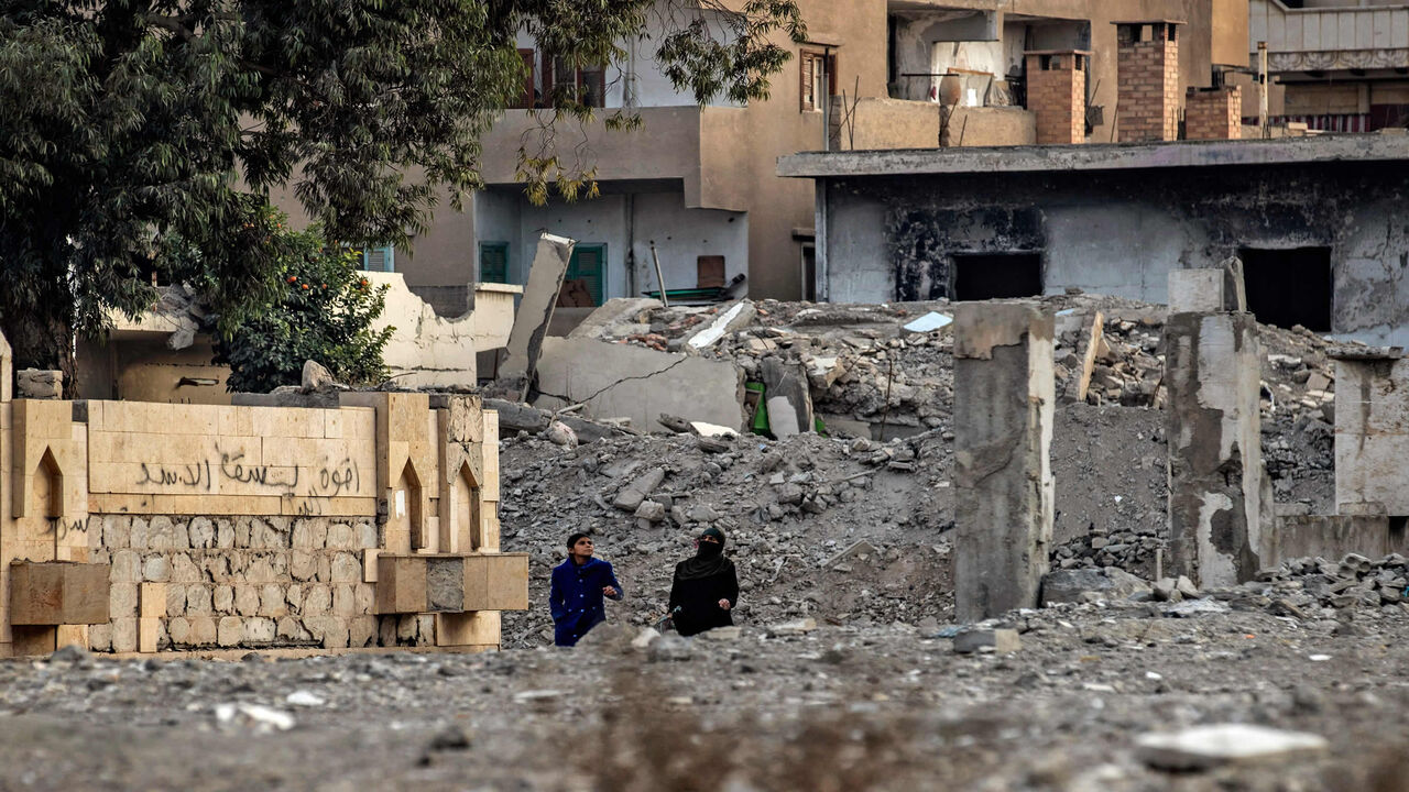 1230242097 Women walk between destroyed buildings in the northern Syrian city of Raqa, the former Syrian capital of the Islamic State (IS) group, on December 20, 2020. - The Kurdish-led Syrian Democratic Forces overran Raqa in 2017, after years of what residents described as IS's brutal rule, which included public beheading and crucifixions. (Photo by Delil SOULEIMAN / AFP) (Photo by DELIL SOULEIMAN/AFP via Getty Images)