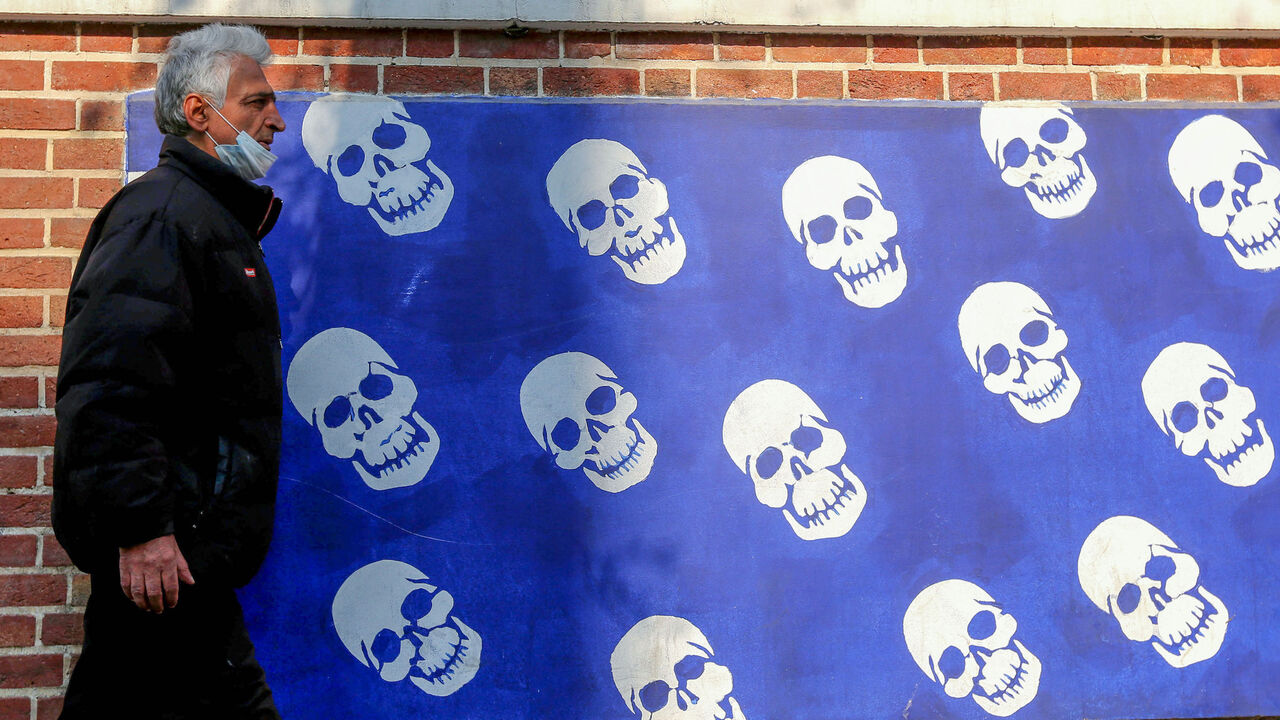 1230355348 An Iranian man wearing a protective mask amid the COVID-19 pandemic, walks past a mural painted on the outer walls of the former US embassy in the capital Tehran, on December 30, 2020. (Photo by ATTA KENARE / AFP) (Photo by ATTA KENARE/AFP via Getty Images)