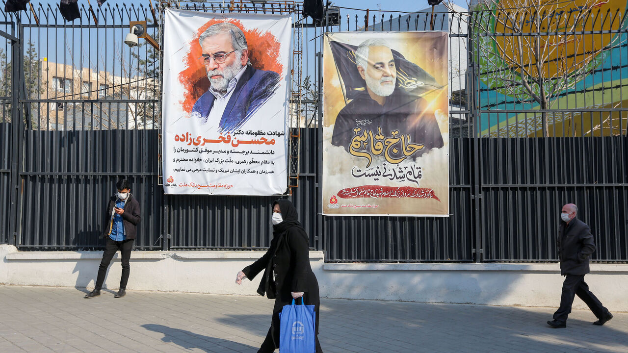 1230355554 Iranians walk past a poster depicting late Revolutionary Guards commander Qasem Soleimani (R) and nuclear scientist Mohsen Fakhrizadeh, assassinated last month, in the capital Tehran, on December 30, 2020. - On January 3, Iraq will mark a year since a US drone strike killed Soleimani, head of the elite external operations of Iran's Revolutionary Guards, alongside Abu Mahdi al-Muhandis, the deputy head of Iraq's powerful Tehran-aligned Hashed Al-Shaabi paramilitary network, nearly sparking a conflict that ma
