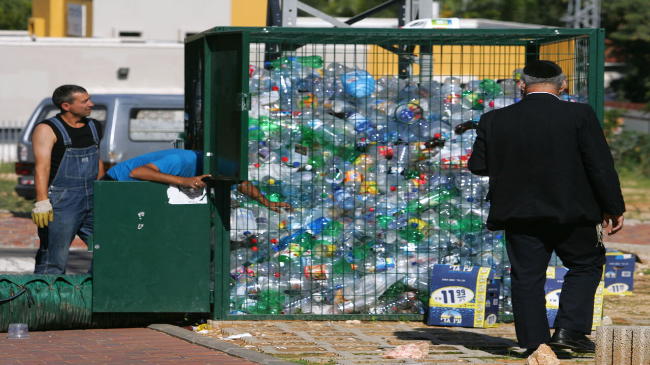 72619475 ROSH HA'AYIN, ISRAEL - NOVEMBER 21: A passing ultra-Orthodox Jew watches as Aviv Recycling workers use a strong vacuum to move plastic bottles from a collection cage into their truck November 21, 2006 in Rosh Ha'Ayin in central Israel. Aviv managers say they recycle about 15 percent of the country's PET plastic waste annually, some 4,000 metric tons or 80 million bottles, but have the capacity to sort, clean, crush and sell more than double that if recycling programs in Israel were more efficient. (Photo b