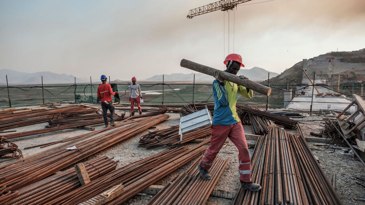 1192325453 A worker walks with a piece of wood on his shoulder at the Grand Ethiopian Renaissance Dam (GERD), near Guba in Ethiopia, on December 26, 2019. - The Grand Ethiopian Renaissance Dam, a 145-metre-high, 1.8-kilometre-long concrete colossus is set to become the largest hydropower plant in Africa.
Across Ethiopia, poor farmers and rich businessmen alike eagerly await the more than 6,000 megawatts of electricity officials say it will ultimately provide.
Yet as thousands of workers toil day and night to finish