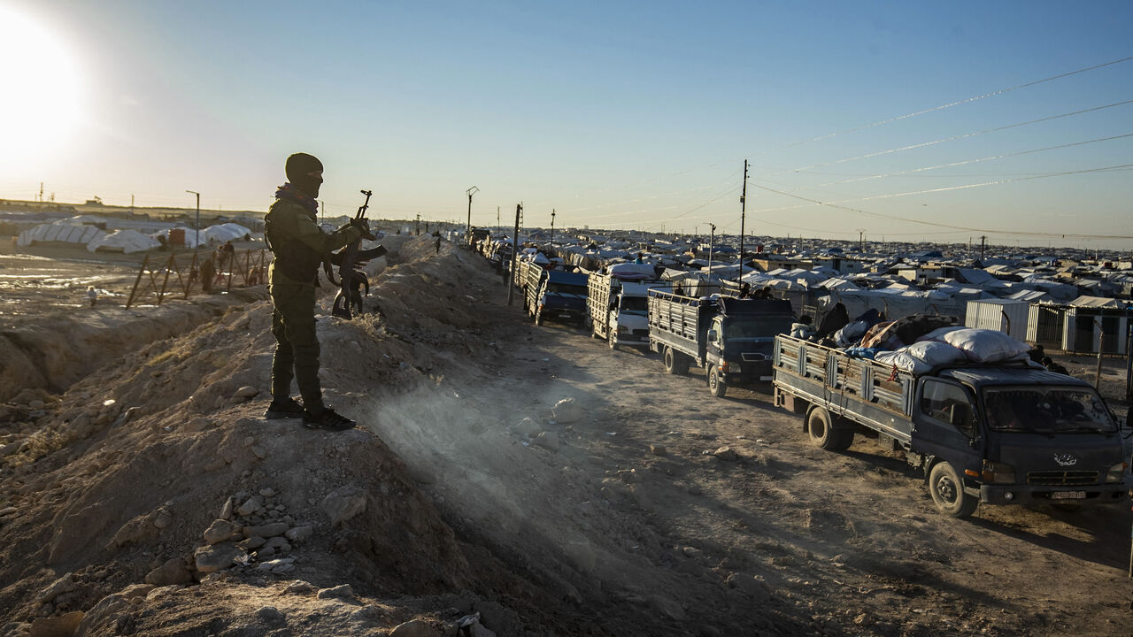 1229768374 TOPSHOT - A masked guard keeps watch as trucks transports Syrians leaving the Kurdish-run al-Hol camp holding relatives of alleged Islamic State (IS) group fighters, in the al-Hasakeh governorate in northeastern Syria, on November 24, 2020. - A Kurdish official in charge of the region's camps, said 515 people from 120 families were returning to areas in the east of Deir Ezzor province, the first to do so after the Kurdish authorities in northeast Syria vowed to allow thousands of Syrians including the famil