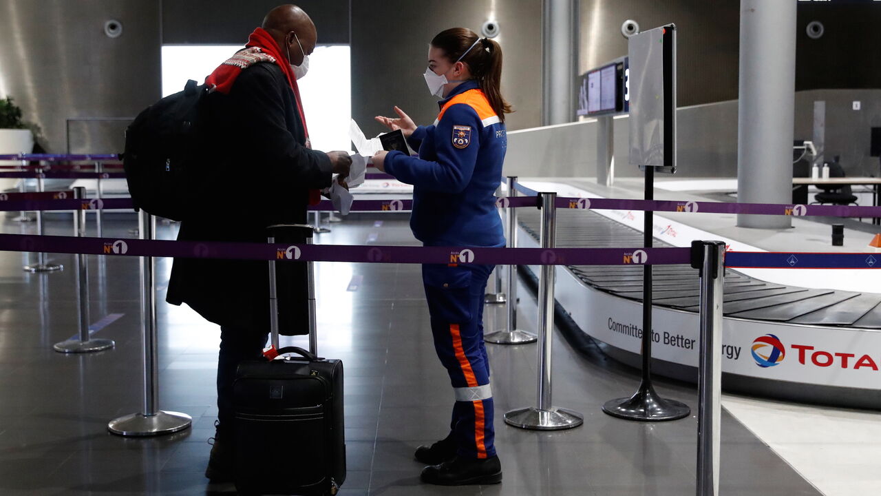 1230985381 A member of the French Civil Defence checks an air traveller's documents at Paris-Charles de Gaulle airport in Roissy, north of Paris, on February 5, 2021, after France implemented tough border restrictions as part of new efforts to contain Covid-19 (novel coronavirus) infections. - France on February 1, 2021, curbed international travel by banning most flights outside the European Union. Only urgent reasons for travel are accepted and border police require written proof before allowing passengers to board.