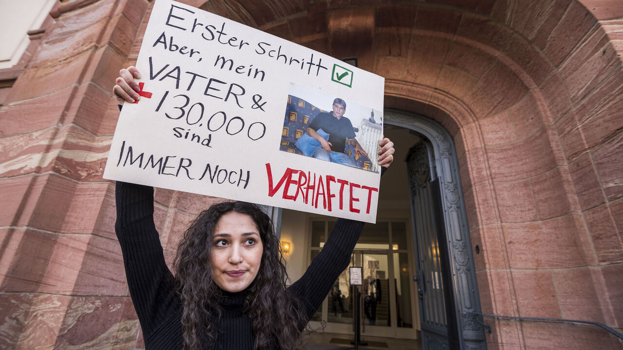 1231353647 Sedra Alshehabi stands with a placard with the picture of her father Ali and a text reading 'First step but my father and 130000 are still in jail' after the verdict in the trail of Syrian defendant Eyad al-Gharib, accused of crimes against humanity in the first trial of its kind to emerge from the Syrian conflict on February 24, 2021 in Koblenz, western Germany. - Eyad al-Gharib, 44, former Syrian intelligence service agent was sentenced to four and a half years in jail for complicity in crimes against hum