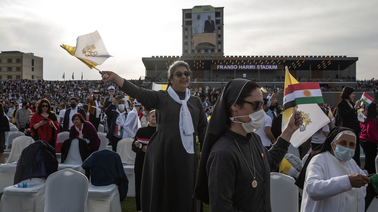 1305838328 ERBIL, IRAQ - MARCH 07: A nun waves a flag as Pope Francis arrives to conduct a mass at the Franso Hariri Stadium on March 07, 2021 in Erbil, Iraq. PPope Francis arrived in Erbil, the final stop of his historic four-day visit, the first-ever papal visit to Iraq. In his first foreign trip since the start of the pandemic, Pope Francis visited Baghdad, Najaf, Erbil, and the cities of Qaraqosh and Mosul, which were heavily destroyed by ISIS. Although the trip is seen as an act of solidarity, the Vatican has bee