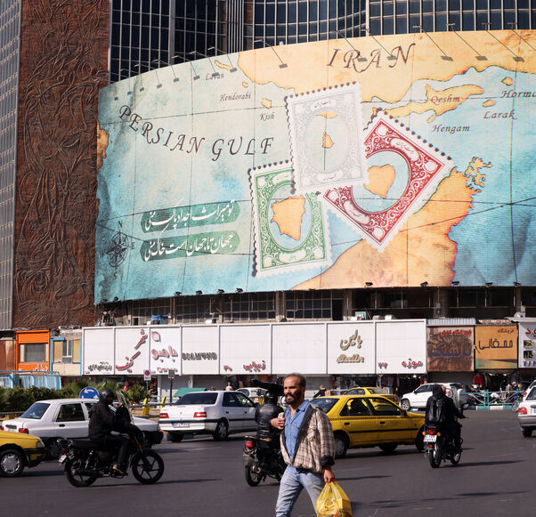 People walk and drive past a billboard covering the facade of a building on Vali-Asr square, depicting as postage stamps the disputed Abu Musa and Greater and Lesser Tunb islands that were seized by Iran in 1971, in Tehran on October 26, 2024. Residents of Tehran awoke and went about their business as planned on October 26 after their sleep was troubled by Israeli strikes that triggered blasts that echoed across the city. (Photo by ATTA KENARE / AFP) (Photo by ATTA KENARE/AFP via Getty Images)