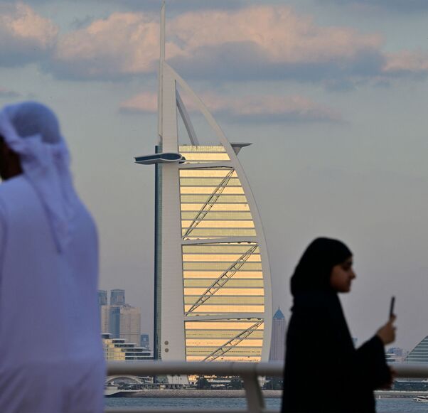 A man and woman walk along a promenade overlooking the Burj al-Arab and Dubai skyline on January 4, 2025. (Photo by Giuseppe CACACE / AFP) (Photo by GIUSEPPE CACACE/AFP via Getty Images)