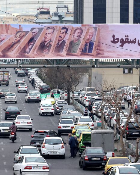 Traffic rolls along a main throughfare under a banner with images of past and present leaders that reads in Farsi, "Domino fall", as daily life returns to the streets following nationwide protests, in the Iranian capital Tehran on January 19, 2026. Demonstrations sparked in late December by anger over economic hardship exploded into protests widely seen as the biggest challenge to the Iranian leadership in years. Limited internet access briefly returned in Iran before dropping again, a monitor said January 