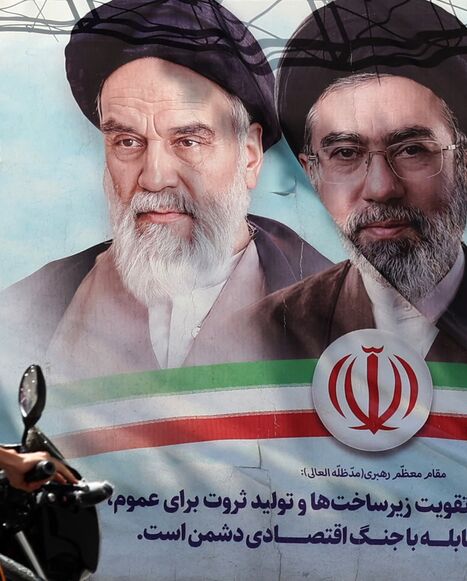 An Iranian man rides his motorbike past a billboard on May 28, 2026.