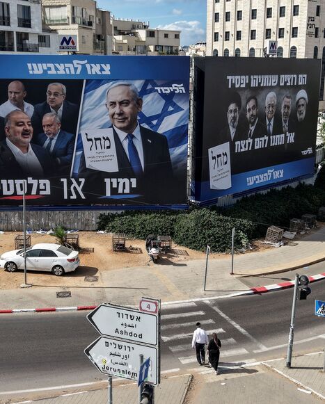 Pedestrians cross a street in front of a banner featuring Israeli Prime Minister Benjamin Netanyahu