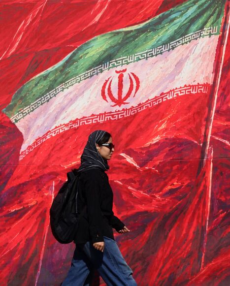 A woman walks past a mural bearing the Iranian national flag
