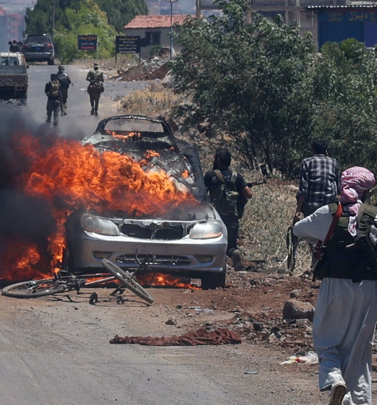 Bedouin and tribal fighters deploy as a car burns at the western entrance of Syria's Druze heartland of Suwayda on July 18, 2025. 