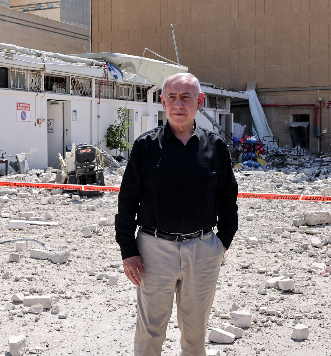 Israeli Prime Minister Benjamin Netanyahu stands amid debris outside the Soroka Hospital in the southern city of Beersheba, after it was hit by a missile fired from Iran on June 19, 2025. Israel's defence minister warned that Iran's supreme leader "can no longer be allowed to exist" after a hospital was hit in an Iranian missile strike on June 19, spiking tensions in the week-old war. (Photo by Marc Israel SELLEM / POOL / AFP) (Photo by MARC ISRAEL SELLEM/POOL/AFP via Getty Images)