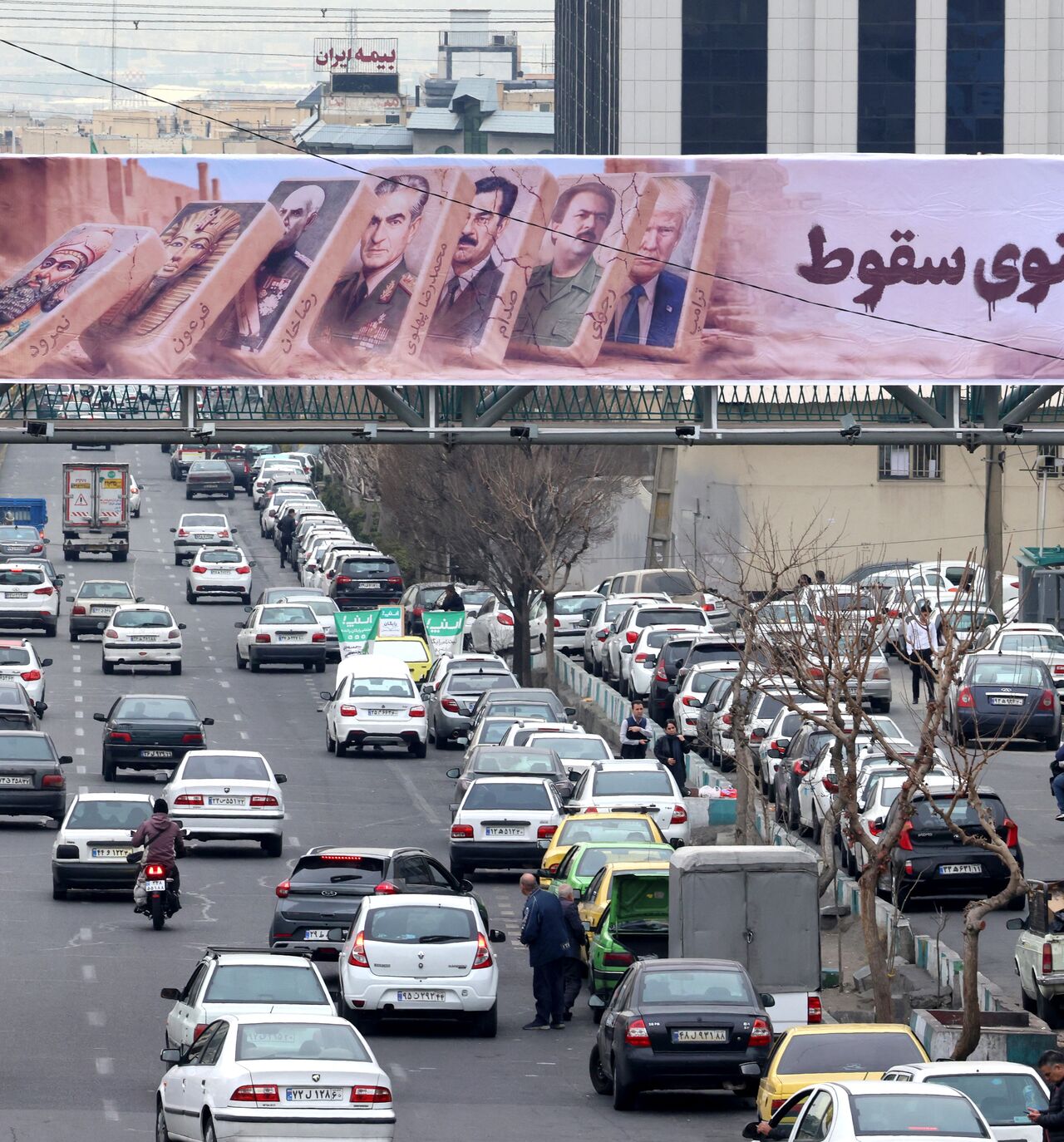 Traffic rolls along a main throughfare under a banner with images of past and present leaders that reads in Farsi, "Domino fall", as daily life returns to the streets following nationwide protests, in the Iranian capital Tehran on January 19, 2026. Demonstrations sparked in late December by anger over economic hardship exploded into protests widely seen as the biggest challenge to the Iranian leadership in years. Limited internet access briefly returned in Iran before dropping again, a monitor said January 