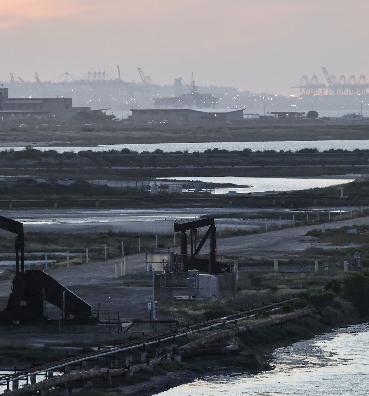 A pumpjack stands idle in the Huntington Beach oil field, with port cranes visible in the distance, on April 23, 2026, in Huntington Beach, California.