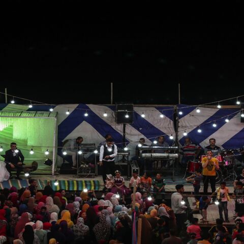 A bride and groom sit on a stage as a band plays music.