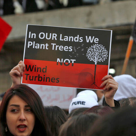 A woman holds up a sign as other protesters wave Syrian national flags and red banners during a demonstration by Druze residents of the village of Majdal Shams in the Israeli-annexed Golan Heights against Israeli construction of wind turbines in the territory, Jan. 24, 2020.