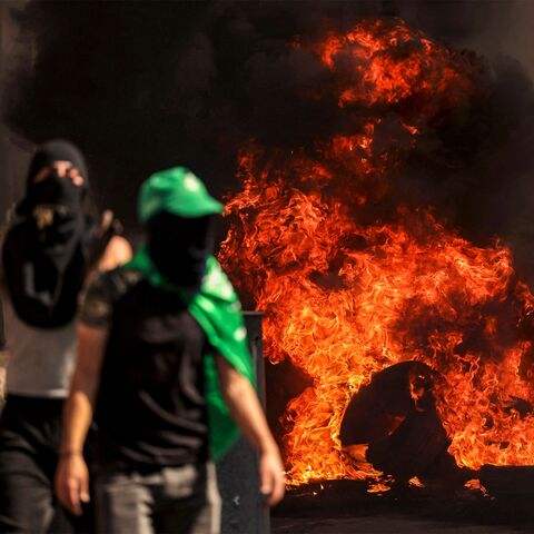 Masked Palestinian protesters walk near flaming tires during clashes with Israeli forces following a rally in solidarity with Gaza by supporters of the Fatah and Hamas movements, in the city of Hebron in the occupied West Bank on October 13, 2023. AFP correspondents and a security official reported clashes after rallies in solidarity with war-battered Gaza in Ramallah, Nablus, Tulkarm, Hebron and other cities and towns, with the Palestinian Red Crescent reporting dozens wounded across the West Bank, some cr