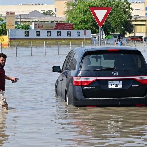 A man walks past a stranded car on a flooded street in Dubai following heavy rains on April 18, 2024.