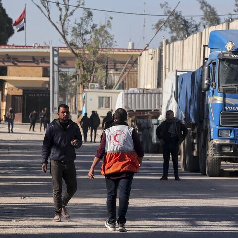 People walk past trucks carrying humanitarian aid that entered Gaza by truck through the Kerem Shalom (Karm Abu Salem) border crossing.