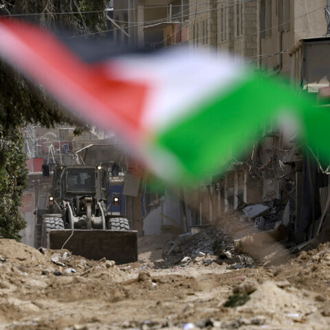 An Israeli army bulldozer digs up a road in the Nur Shams refugee camp in Tulkarem with a Palestinian flag fluttering in the foreground on the second day of a large-scale military operation in the north of the occupied West Bank on August 29, 2024. The death toll climbed on August 29 as the Israeli army said it killed five militants in Tulkarem, bringing to 14 the overall number of people killed since the launch of the West Bank operation the previous day. (Photo by Jaafar ASHTIYEH / AFP) (Photo by JAAFAR A