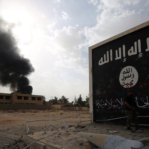 Iraqi fighters of the Hashed al-Shaabi stand next to a wall bearing the Islamic State (IS) group flag as they enter the city of Al Qaim as they fight against remnant pockets of Islamic State group jihadists on November 3, 2017. 