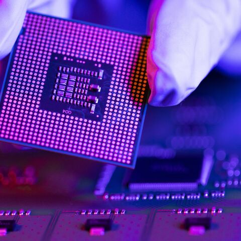 An engineer holds a CPU chip against the background of a motherboard.