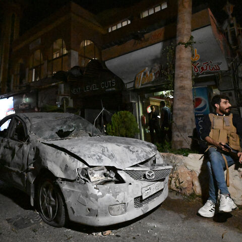 An armed man sits in front of a car damaged in a reported Israeli strike in Damascus on Oct. 2, 2024.