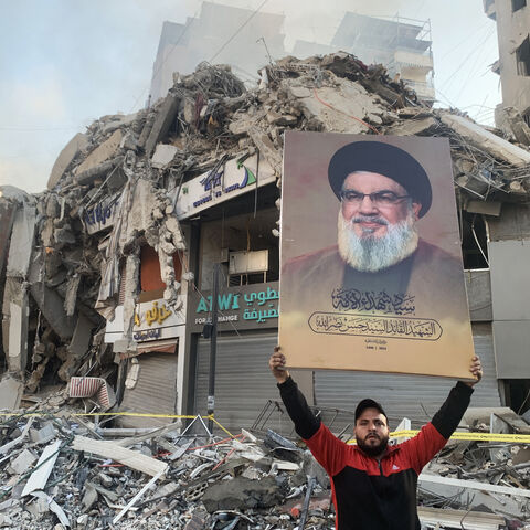 A man flashes a portrait of slain Hezbollah chief Hassan Nasrallah in front of the rubble of a building at the site of an Israeli airstrike in Beirut's southern suburbs, on November 12, 2024, amid the ongoing war between Israel and Hezbollah. (Photo by AFP) (Photo by -/AFP via Getty Images)