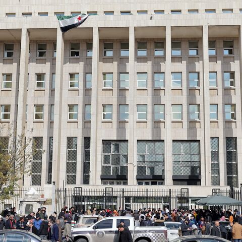 Vehicles move past as people queue outside the main headquarters of the Central Bank of Syria to exchange US dollars at prices lower than the black market.