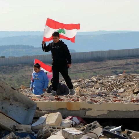 Lebanese children hold their national flag as they walk above the rubble of a destroyed building as families return with the Lebanese army to the southern village of Marwahin, near a border fence with Israel, on Jan. 28, 2025. 