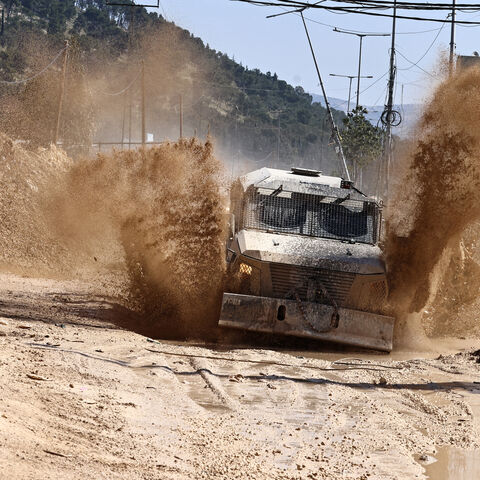 A journalist tries to avoid mud splatter as Israeli forces drive on a destroyed road in the Nur Shams camp for Palestinian refugees near Tulkarem, after reportedly issuing demolition notifications for several houses amid a weeks-long offensive in the occupied West Bank on February 26, 2025. (Photo by Zain JAAFAR / AFP) (Photo by ZAIN JAAFAR/AFP via Getty Images)