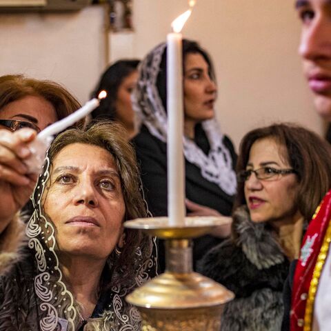 A woman reaches to light her candle from another held by deacon during the Christmas morning mass at the Syriac Orthodox Church of Virgin Mary in the Kurdish-majority city of Qamishli in Syria's northeastern Hasakeh province on Dec. 25, 2022. 