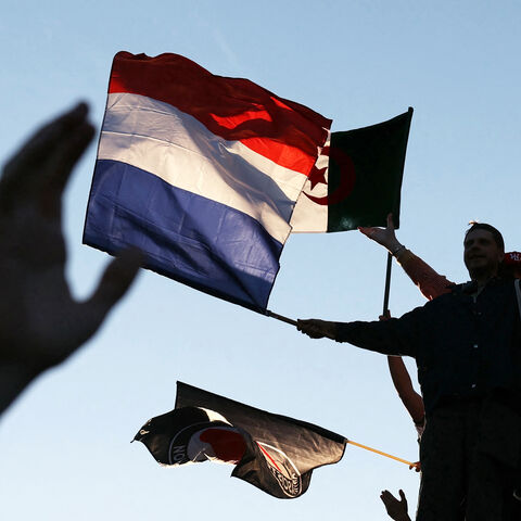 Attendees fly a French national flag and an Algerian national flag during a gathering for the election night following the second round results of France's legislative election at Republique Square in Paris on July 7, 2024. A broad left-wing coalition was leading a tight French legislative election, ahead of both President's centrists and the far right with no group winning an absolute majority, projections showed. (Photo by Alain JOCARD / AFP) (Photo by ALAIN JOCARD/AFP via Getty Images)