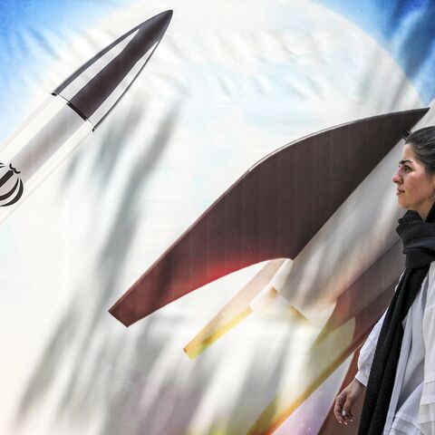 A woman walks past a banner depicting launching missiles bearing the emblem of the Islamic Republic of Iran in central Tehran on April 15, 2024.