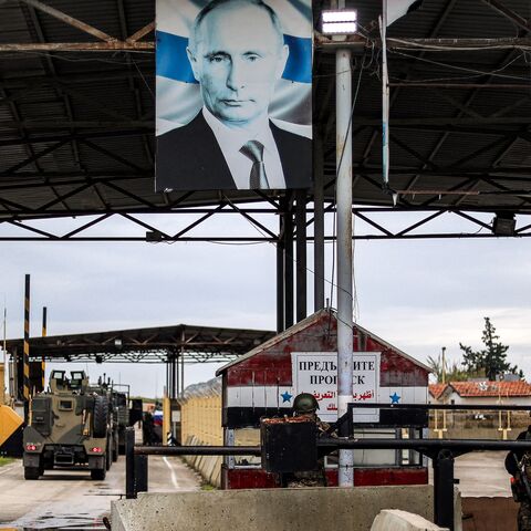 A portrait of Russia's President Vladimir Putin hangs above next to a torn out one of the ousted Syrian president, as Russian soldiers stand guard at the entrance of the Russian-leased Syrian military base of Hmeimim in Latakia province in western Syria on December 29, 2024.