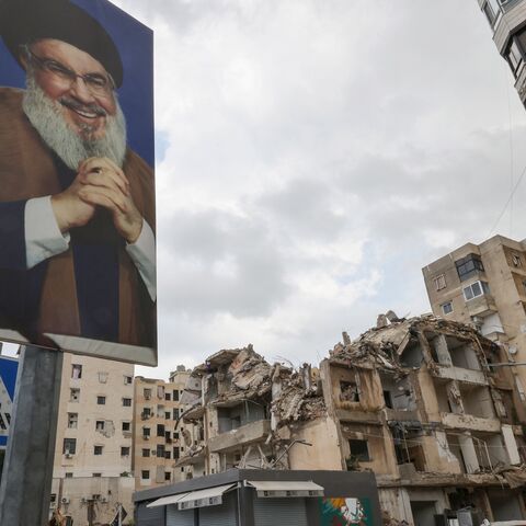 People drive on a street past portraits of slain Lebanese Hezbollah leader Hassan Nasrallah and buildings damaged in Israeli strikes in the recent war in the Ghobeiry neighborhood of Beirut's southern suburb on May 4, 2025.