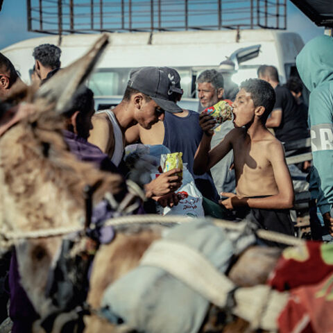 A hungry young boy eats raw noodles as dislocated Palestinians carry the humanitarian aid they have received from a United Nations distribution point in Rafah, southern Gaza Strip on May 27, 2025, following a chaotic incident in which Gazans stormed the aid center, leading to the withdrawal of the American company overseeing the operation after losing control of the situation. The scene underscores the desperation and urgency surrounding the humanitarian crisis as