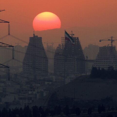 Sun setting at the back of large buildings under construction of Tehran at dusk.