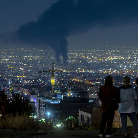 People gather on a hill to watch smoke rising in the distance from an Israeli airstrike in Tehran, Iran, on June 14, 2025.