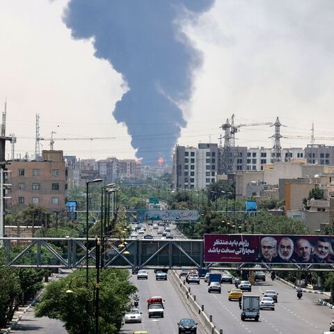 Portraits of Iranian military generals and nuclear scientists, killed in Israel's June 13 attack are displayed above a road, as a plume of heavy smoke and fire rise from an oil refinery in southern Tehran, after it was hit in an overnight Israeli strike, on June 15, 2025.