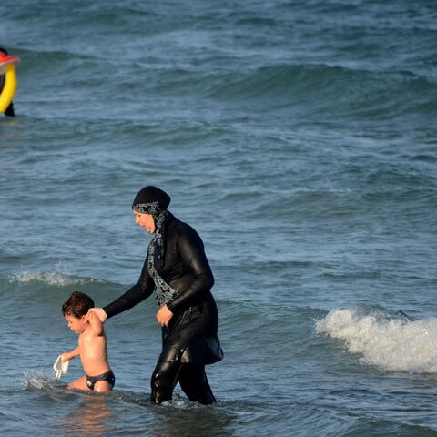 A Tunisian woman wearing a "burkini", a full-body swimsuit designed for Muslim women, walks in the water with a child on August 16, 2016 at Ghar El Melh beach near Bizerte, north-east of the capital Tunis. (Photo by FETHI BELAID / AFP) (Photo by FETHI BELAID/AFP via Getty Images)